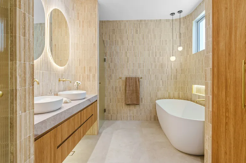 Bagno con piastrelle chiare, mobile in legno con due lavabi da appoggio, specchio ovale e vasca